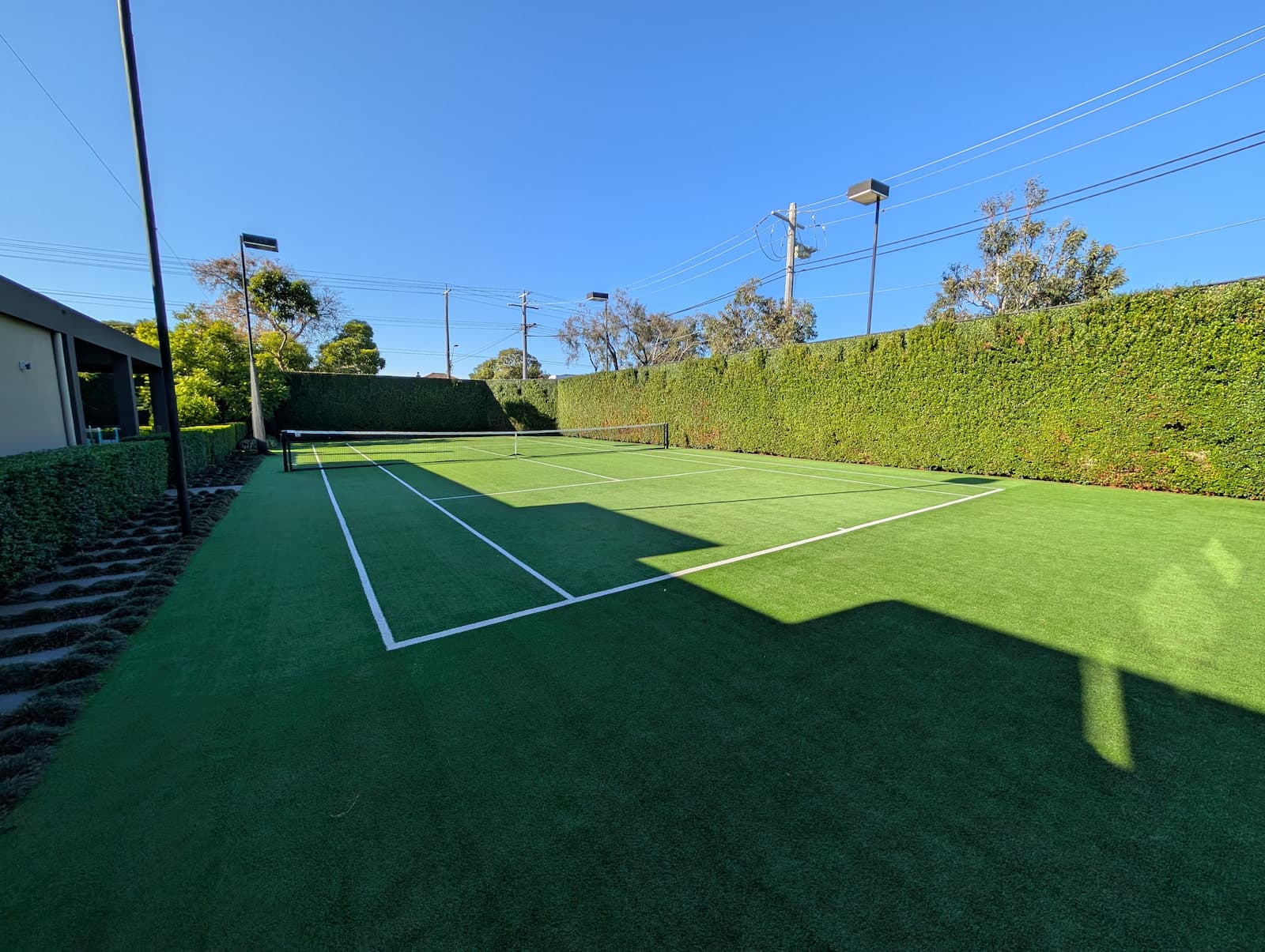An artificial turf court installation bordered by a neatly trimmed hedge