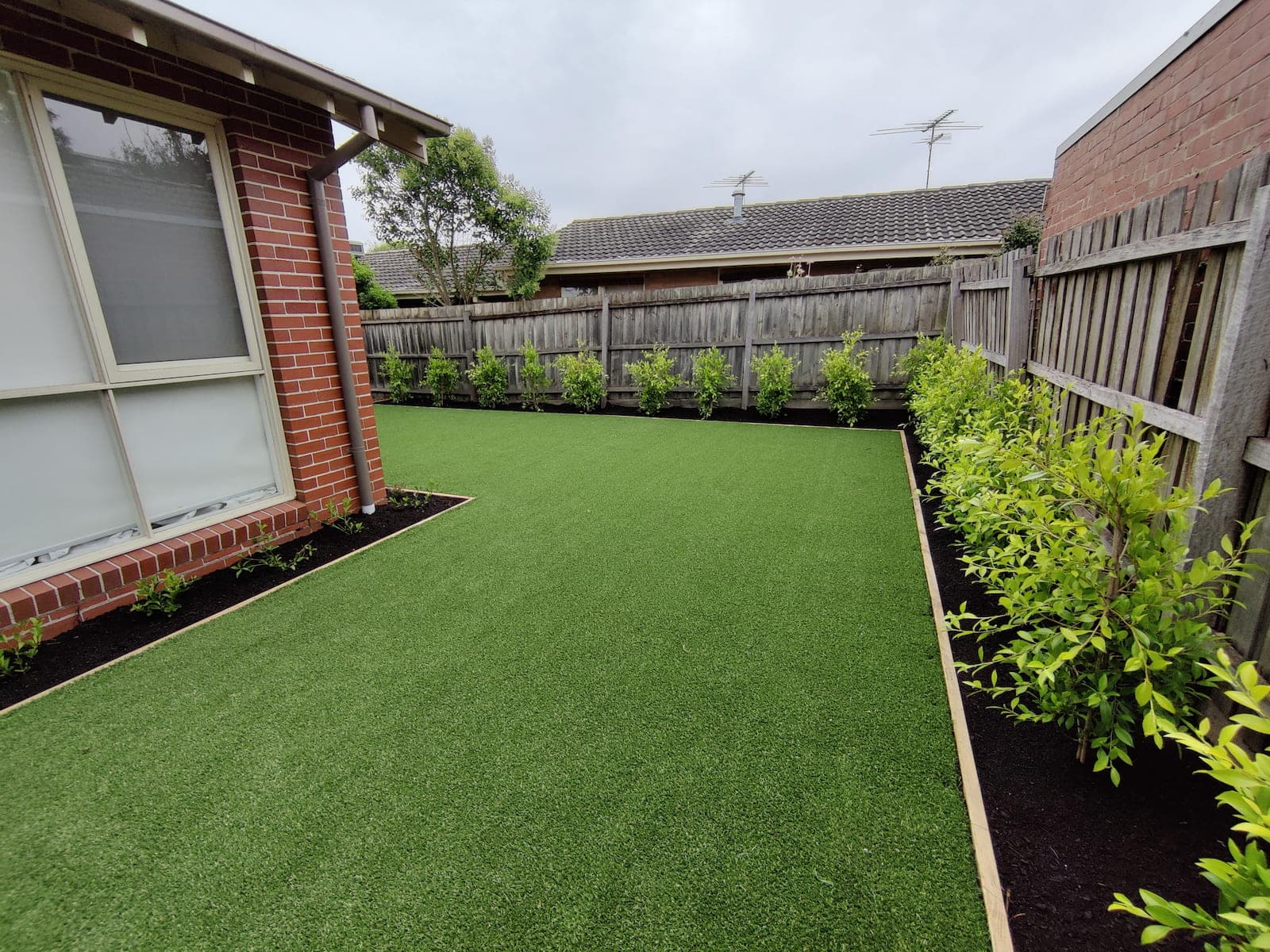 Artificial turf installation with new garden bed plantings along the fence line